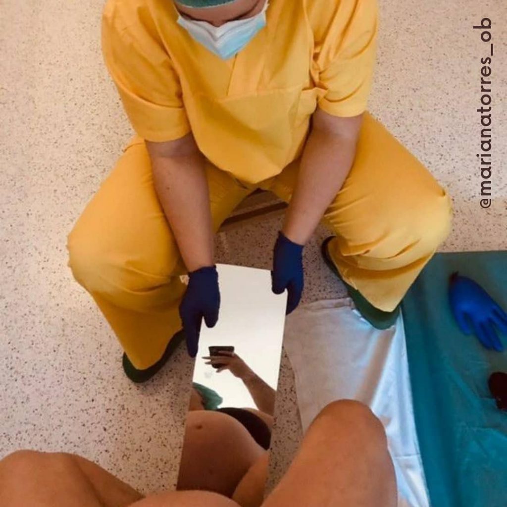 grávida sentada no parto a ver o bebé nascer através de um espelho segurado pela obstetra