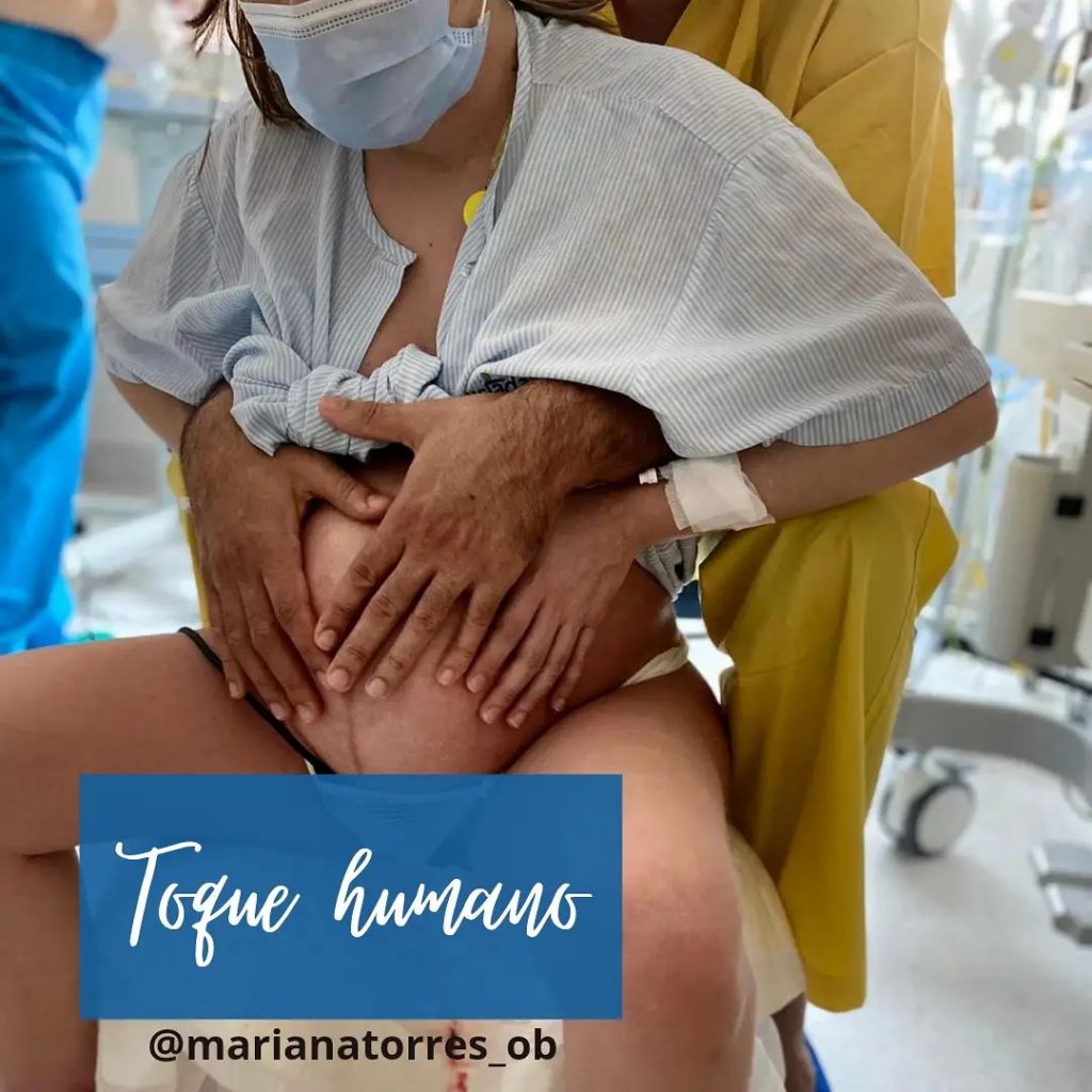 gravida num banco de parto encostada ao companheiro que tem as mãos sobre a sua barriga